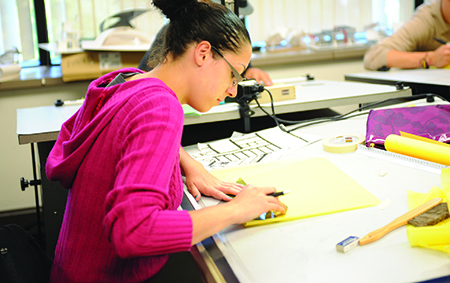 A student working on an architectural design on paper.